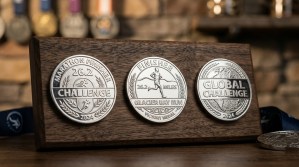 Three polished silver race challenge coins with marathon distance inscriptions and finisher text on a runner medal display board